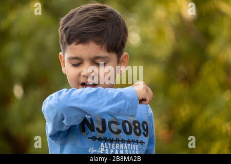 Il bambino indiano tosse sul suo gomito che mostra le punte per proteggere il virus della corona Foto Stock