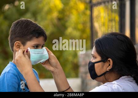 Madre aiutare bambino a indossare maschera in india per proteggerlo contro l'influenza e il virus Foto Stock