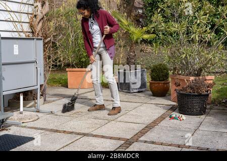 Giovane donna che puliscono fogliame sulla terrazza in primavera. Foto Stock