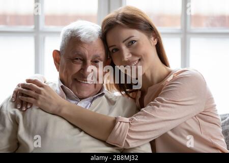 La nipote di Grownup che si prende cura abbraccia il nonno degli anziani 75 seduti sul divano Foto Stock
