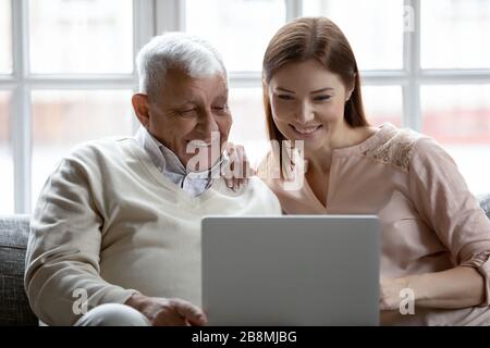 La figlia di Grownup e il padre degli anni '80 si siedono sul divano con il computer portatile Foto Stock
