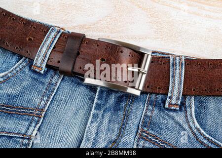 Jeans con cintura in vera pelle marrone con fibbia classica in metallo su fondo in legno. Eleganti accessori in pelle da uomo. Vista dall'alto. Foto Stock