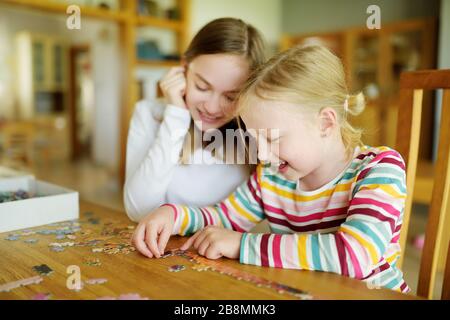 Carino ragazze giovani giocare puzzle a casa. I bambini che collegano i pezzi del puzzle del puzzle in un tavolo del soggiorno. I bambini che assemblano un puzzle. Famiglia divertente Foto Stock