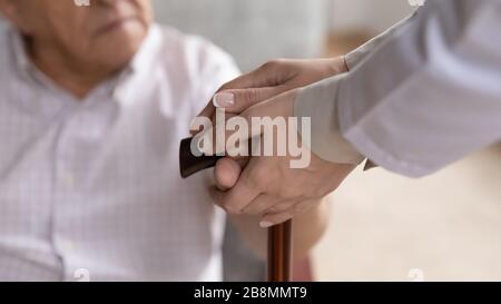 Le mani del caregiver che tengono le vecchie braccia del paziente toccano il bastone da camminare in primo piano Foto Stock