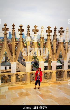 Donna turistica in rosso visita e ammirando la vista e le guglie e statue sul tetto della Cattedrale di Milano in primavera piovosa giorno, Italia, maggio 2017 Foto Stock