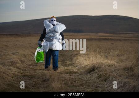 Perthshire Hills, Regno Unito. 22 marzo 2020. Nella foto: Immagine concettuale di una persona che va a lunghezze estreme per autoisolarsi nel mezzo del nulla che trasporta l'articolo più ricercato nel mondo della carta igienica, mentre avvolto in casa ha fatto dispositivi di protezione personale. Credit: Colin Fisher/Alamy Live News Foto Stock