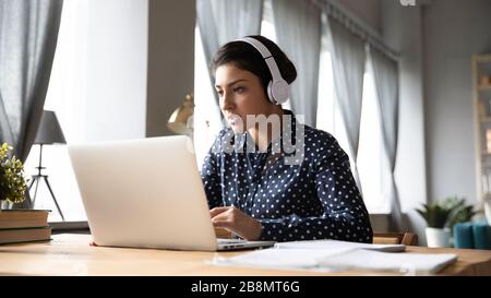 Giovane e occupata donna indiana che indossa le cuffie e lavora sul laptop Foto Stock