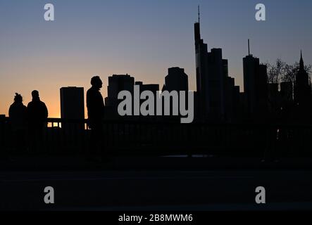 22 marzo 2020, Hessen, Francoforte sul meno: I passanti guardano il tramonto nella città bancaria sul ponte di zattera. In risposta alla diffusione del coronavirus, alcuni stati federali hanno limitato la vita pubblica. Foto: Arne Dedert/dpa Foto Stock