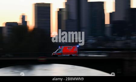 22 marzo 2020, Hessen, Francoforte sul meno: Un'ambulanza guida sopra il ponte di Ignatz-Bubis con luce blu al tramonto nella città bancaria. In risposta alla diffusione del coronavirus, alcuni stati federali hanno limitato la vita pubblica. Foto: Arne Dedert/dpa Foto Stock