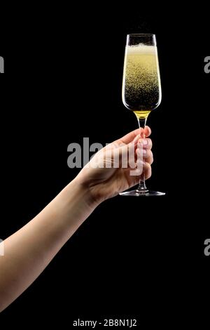 Donna mano che tiene un bicchiere di champagne frizzante isolato su nero. Foto Stock