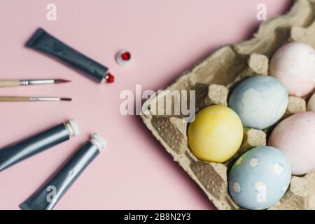 Il concetto di colorare le uova di Pasqua in colori pastello acquerelli. Vernici e pennelli per colorare le uova per Pasqua su sfondo rosa. Foto Stock