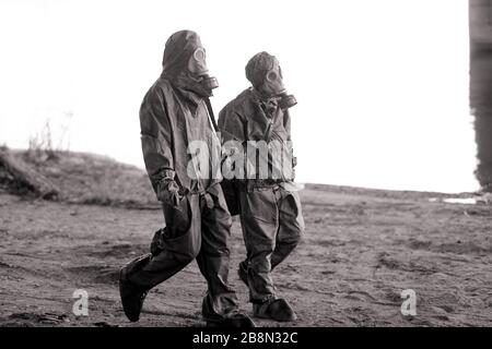 Due persone camminano in tute protettive NBC e maschere a gas. Concetto di misure preventive e di protezione per il coronavirus COVID 19 pandemico e altri g Foto Stock