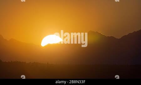 The sun peeks behind the Olympic Mountains as it sets for the evening casting a golden glow on the sky and mountain range Foto Stock