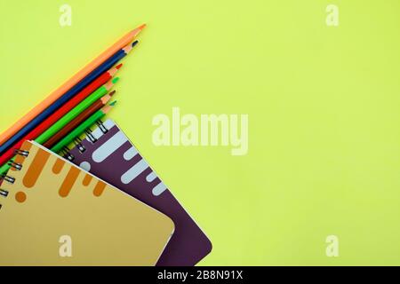 Materiali di studio contenenti sei pastelli di matita di legno e due quaderni di carta sparsi su uno sfondo di carta Foto Stock