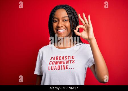 Giovane african american donna che indossa sarcasm coments testo su t-shirt su sfondo rosso facendo ok segno con le dita, simbolo eccellente Foto Stock