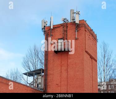 Apparecchiature per la comunicazione cellulare e la trasmissione dati. Antenne 2G, 3G, 4G, 5G installate sul tetto di una vecchia torre d'acqua in mattoni Foto Stock