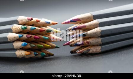 Un'immagine di primo piano di due serie opposte di matite colorate su uno sfondo grigio Foto Stock