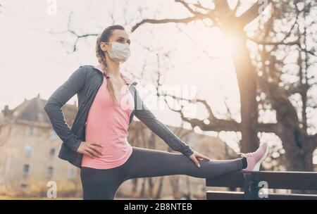 Donna che indossa maschera facciale stretching su una panca all'aperto Foto Stock