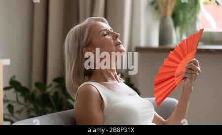 Signora più vecchia sudata usando la ventola di ondulazione della carta. Foto Stock