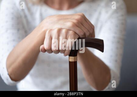 Primo piano donna più anziana tenendo le mani grinze su bastone di legno da passeggio. Foto Stock