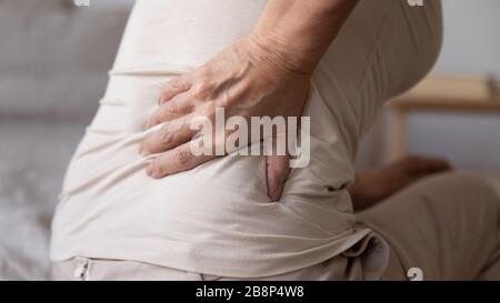Primo piano donna anziana in pensione toccando la parte inferiore posteriore. Foto Stock