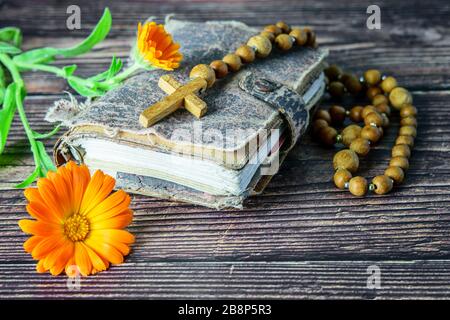 Croce di legno con cappelletto sull'antica bibbia e un fiore sullo sfondo di legno. Religione cristiana. Noi abbiamo fiducia in dio. Foto Stock