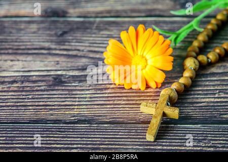 Croce cristiana con cappelletto e fiore in primo piano su sfondo ligneo. Simbolo della religione cristiana. Foto Stock