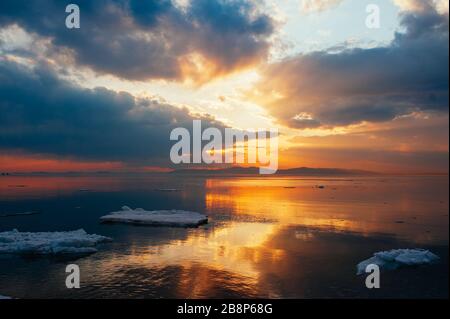 Incredibile e bellissimo tramonto sul mare sullo sfondo delle montagne. Mare acqua calma in cui il ghiaccio si fonde e piccoli pezzi di ghiacciai galleggiano. Foto Stock
