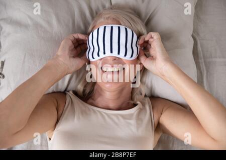 Donna sorridente di mezza età che indossa la maschera del sonno. Foto Stock