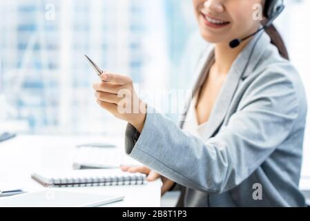 Donna addetto al telemarketing che punta mano mentre lavora in ufficio Foto Stock