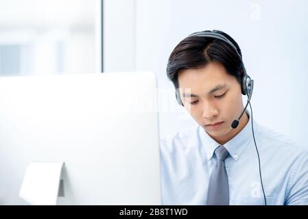 Personale di telemarketing asiatico che indossa cuffie e auricolari, concentrandosi sul lavoro in ufficio Foto Stock