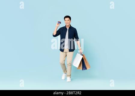 Bel giovane turista asiatico che trasporta borse shopping con carta di credito isolato su sfondo azzurro Foto Stock