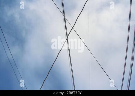 Intreccio di fili e cavi contro il cielo blu con nuvole. Paesaggio urbano industriale. Foto Stock