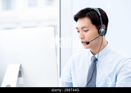 Portait di giovane bell'agente di call center asiatico che guarda il computer che lavora in ufficio Foto Stock