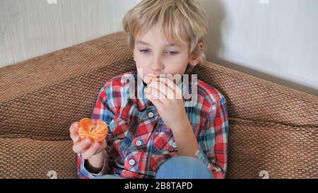 Il ragazzo di otto anni mangia il mandarino a casa Foto Stock