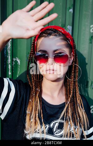 Studentessa elegante in occhiali da sole chiude la sua mano dal sole luminoso, guarda in lontananza, una calda giornata di sole Foto Stock