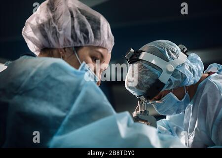 Personale chirurgico in sala operatoria, primo piano. Un team internazionale di medici professionisti in una moderna sala operatoria è in fase di intervento chirurgico. Salvataggio Foto Stock