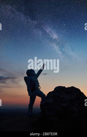 Silhouette di viaggiatori spaziali in piedi su una montagna rocciosa e puntando alle stelle, Milky Way. Cosmonauta che indossa la tuta spaziale bianca mentre guarda il fantastico cielo stellato. Concetto di galassia, umana nello spazio Foto Stock