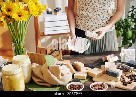 Immagine ritagliata di donna che impacchettano saponette fatte a mano in confezioni di cartone per la vendita Foto Stock