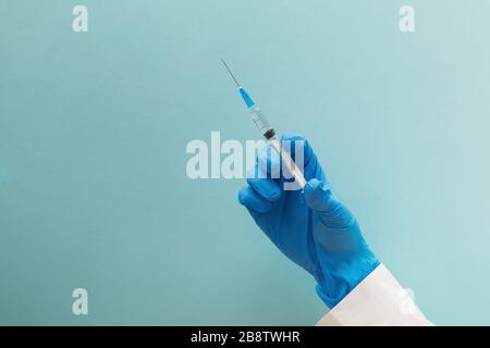 Mano con guanti blu che tengono la siringa isolata su sfondo blu Foto Stock