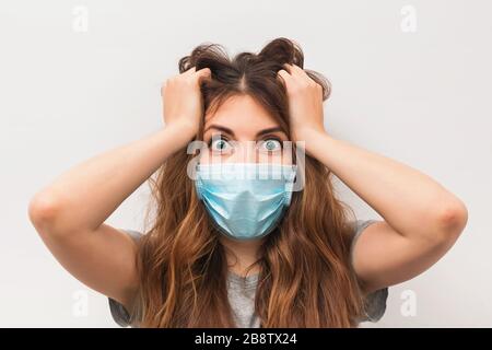 Giovane donna spaventa in maschera medica che si trova sopra la parete bianca Foto Stock