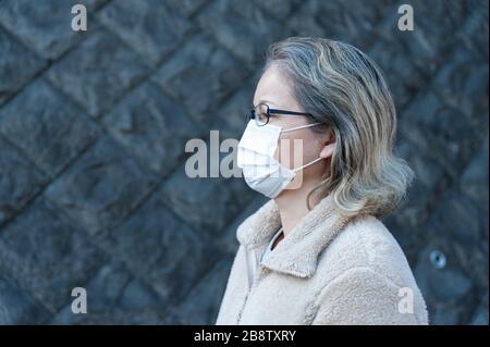 Donna 40-49 anni all'aperto con occhiali e maschera bianca per proteggere contro virus, influenza, febbre da fieno e altre malattie. Guardando al lato. Foto Stock