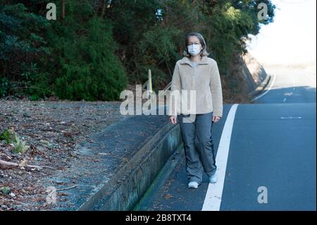 Donna 40-49 anni all'aperto con occhiali e maschera bianca per proteggere contro virus, influenza, febbre da fieno e altre malattie. Camminando sulla strada. Foto Stock