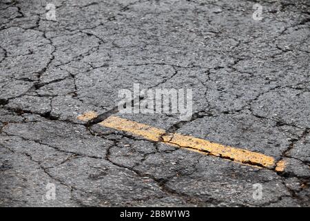 Strada asfaltata rotta con linea di demarcazione gialla. Texture di sfondo astratta per il trasporto Foto Stock