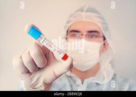 un giovane scienziato indaga un esame del sangue per il coronavirus. Diagnostica 2019-ncov. Risultato positivo del test del sangue per covid 19. Medico caucasico con un b Foto Stock