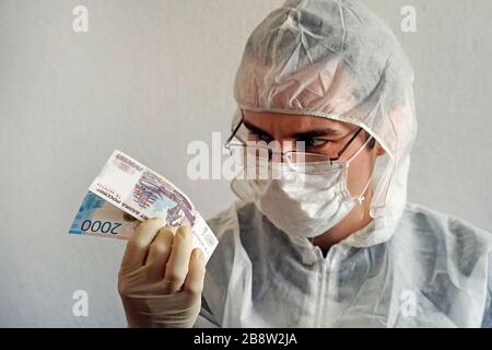 Uno scienziato in un vestito protettivo e guanti medici e maschera tiene in mano denaro. Germi di sporcizia e batteri di virus sul denaro. Foto Stock