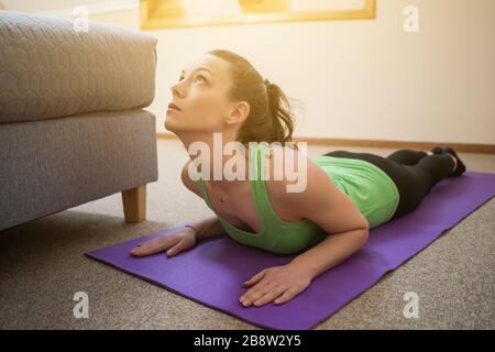 La giovane donna pratica lo yoga a casa. Bhujangasana / posa Cobra Foto Stock