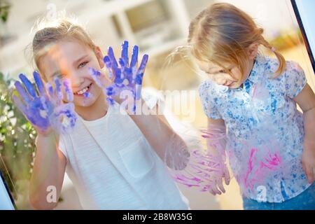 I bambini disegnano le impronte digitali su un vetro con le loro pitture per le dita e le mani Foto Stock