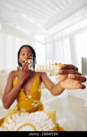 Sorpresa giovane donna che copre la bocca con la mano quando si guarda il test elettronico di gravidanza in mano Foto Stock