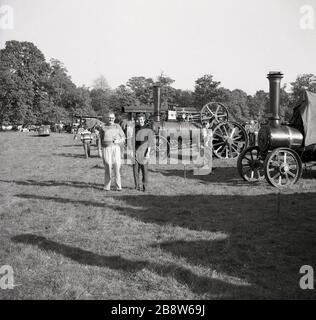 1963, storico, fuori in piedi in un campo erboso, un padre e un figlio che visitano un rally a vapore, Inghilterra, Regno Unito. Foto Stock